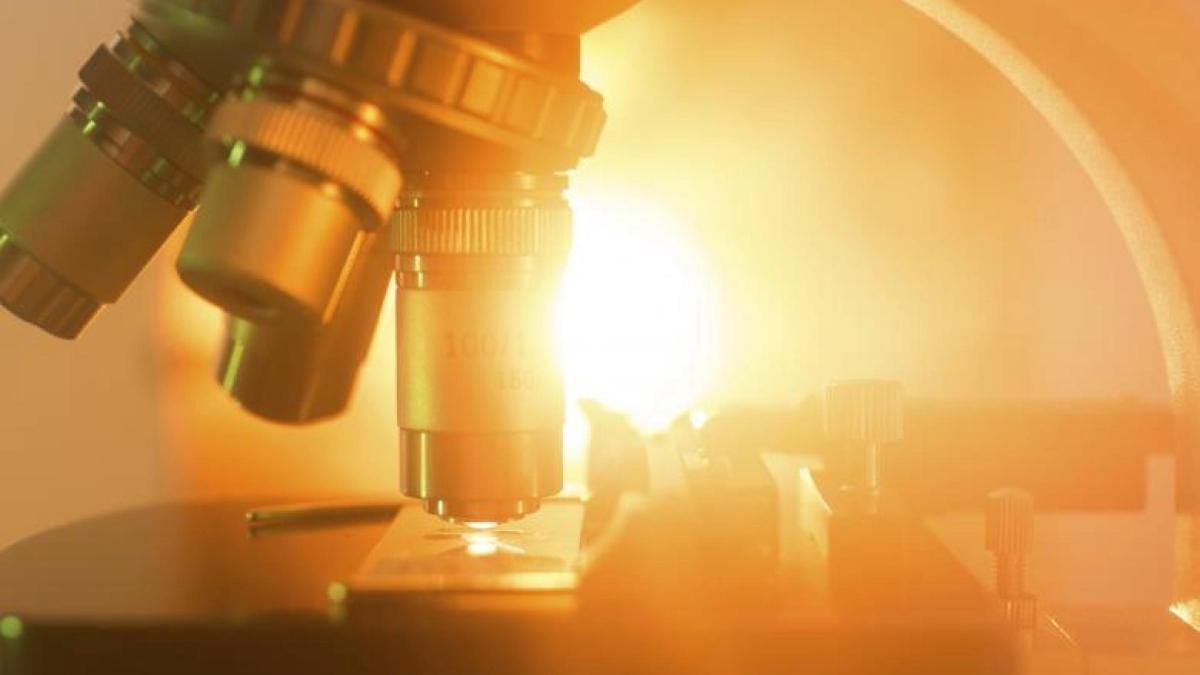 Close up of microscope with an orange light in the background.