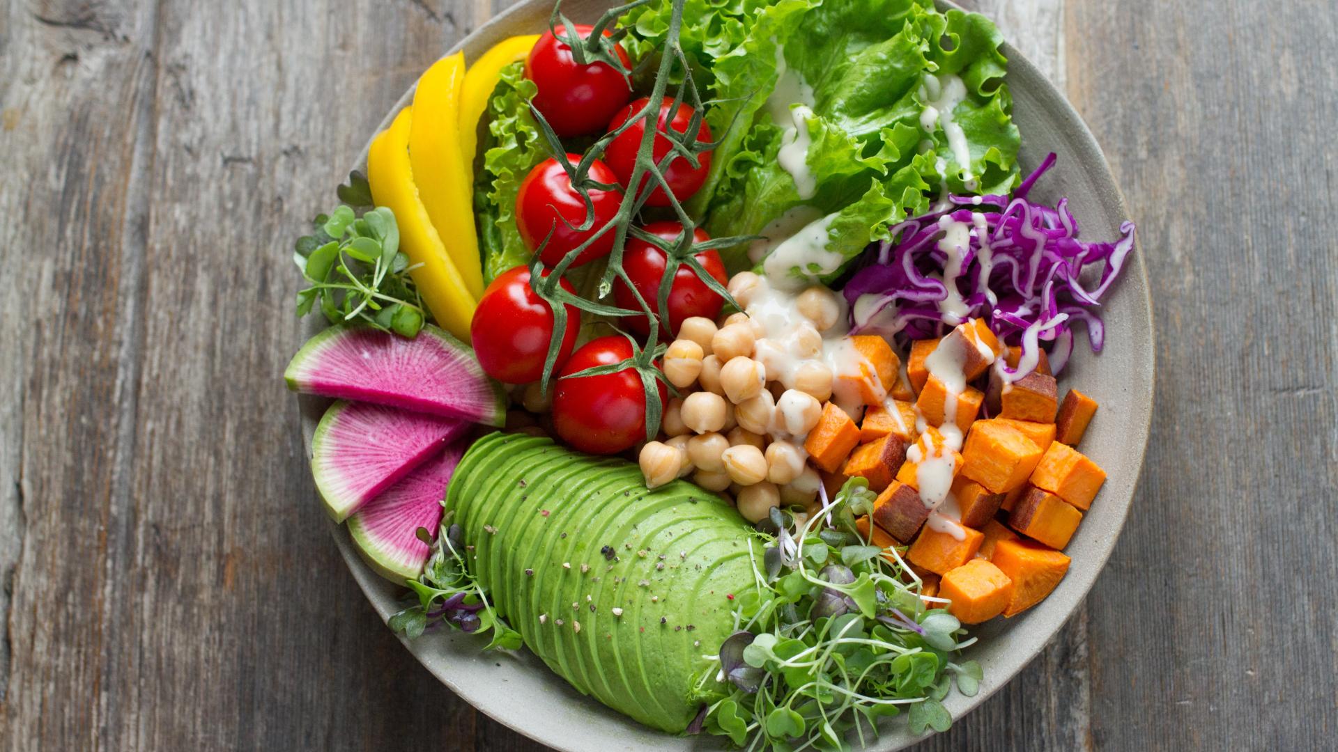 Colorful salad bowl with fresh vegetables: avocado, cherry tomatoes, chickpeas, sweet potato, and greens.