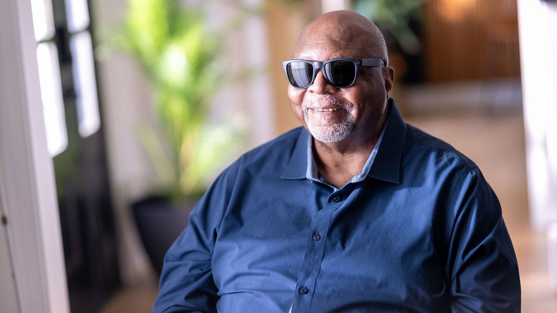 Man in blue shirt and sunglasses smiling at the camera