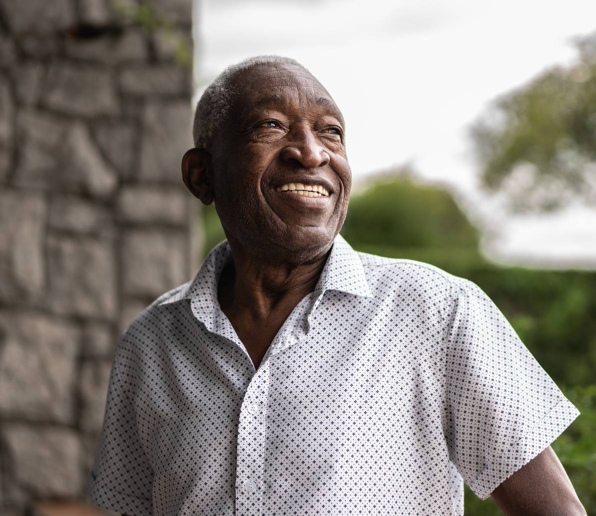 Smiling older man standing outdoors in sunlight.