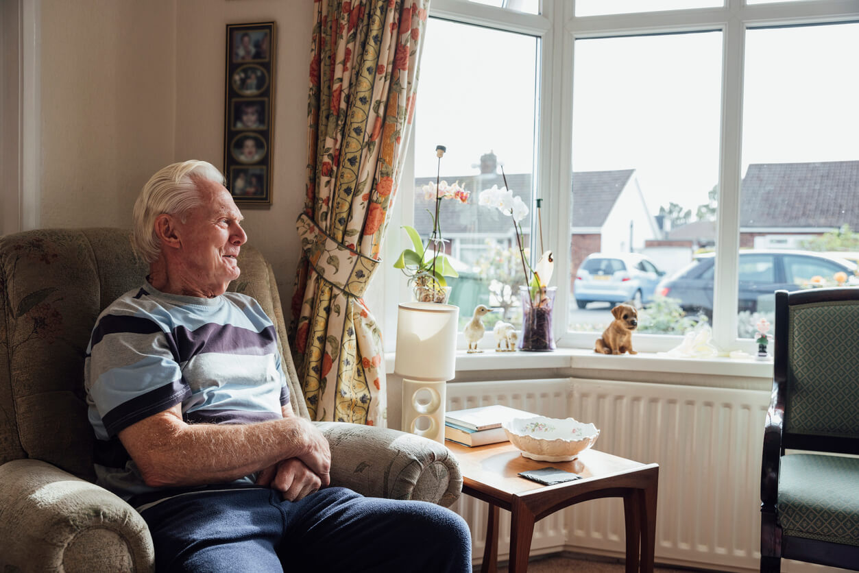 Side view of a senior man who has a chronic illness/Alzheimer's disease sitting in a living room at his home in the North East of England.