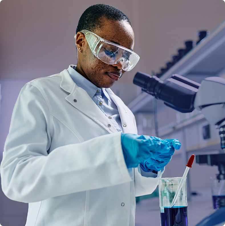 A scientist in a white lab coat, protective goggles, and blue gloves, carefully working with a specimen in a laboratory setting.