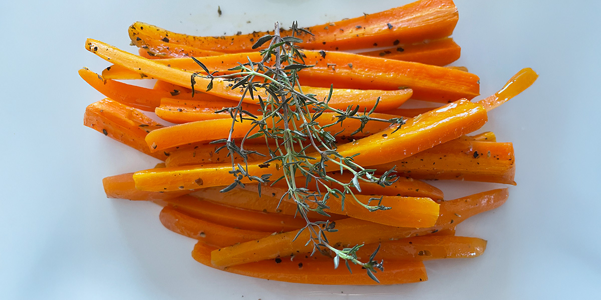 A picture of carrots, sliced thinly, in a pile with a line of dried green herbs crossing them.