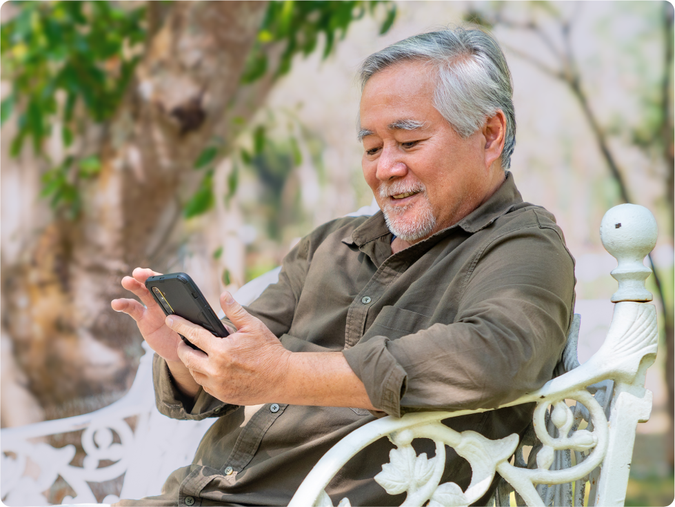 Older man sitting outdoors on a bench using a smartphone to read messages