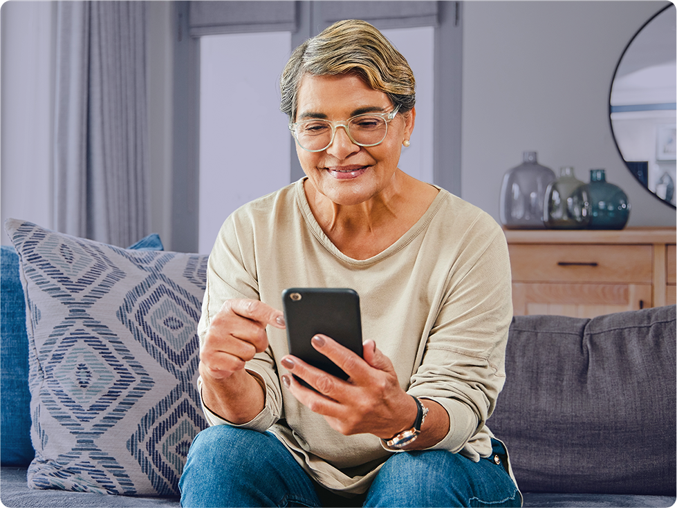 Two women, one younger and one older, are sitting together, smiling and looking at a smartphone.