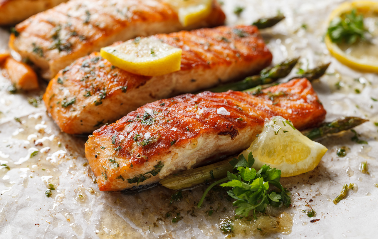 Baked salmon fillet and asparagus with aromatic herbs and lemon on baking paper close up view