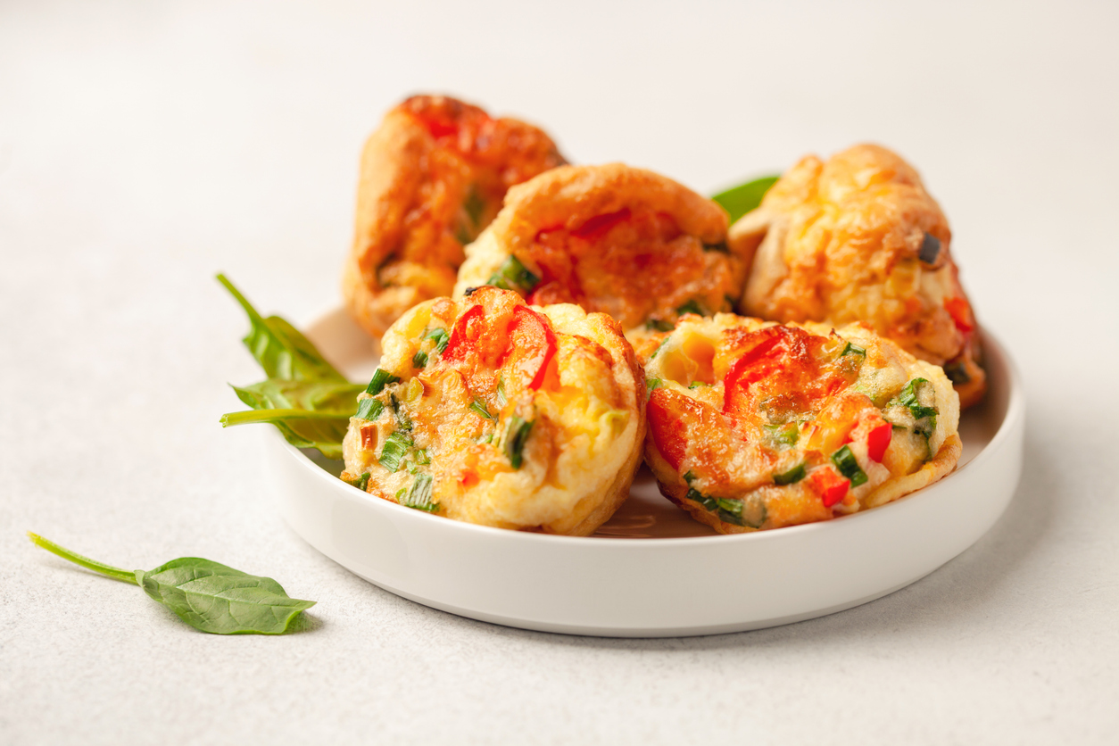 Egg bites with red peppers and spinach on a white high-sided plate against a gray background