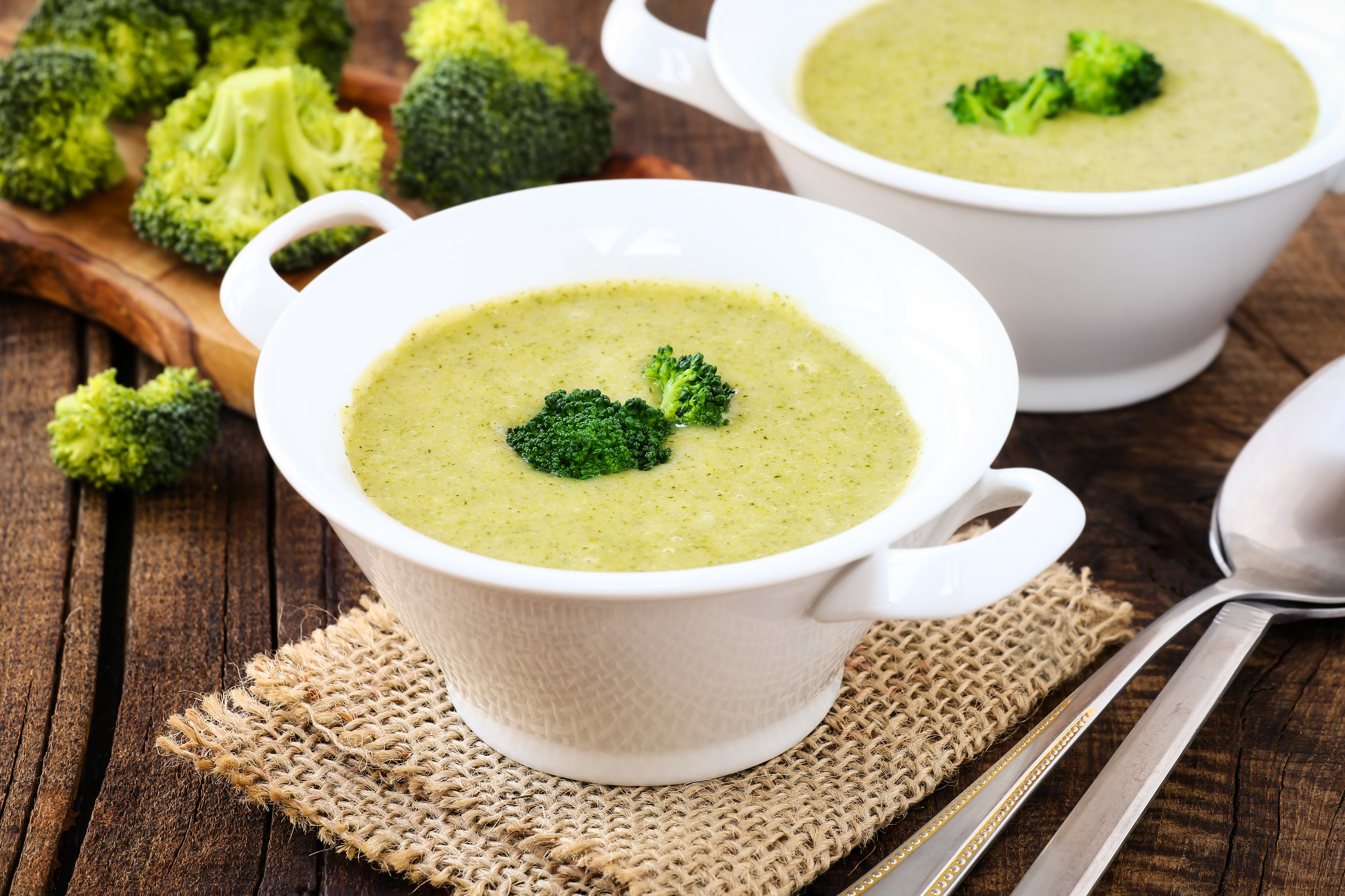 Healthy vegetarian cream of broccoli soup in white bowls on a rustic kitchen table.